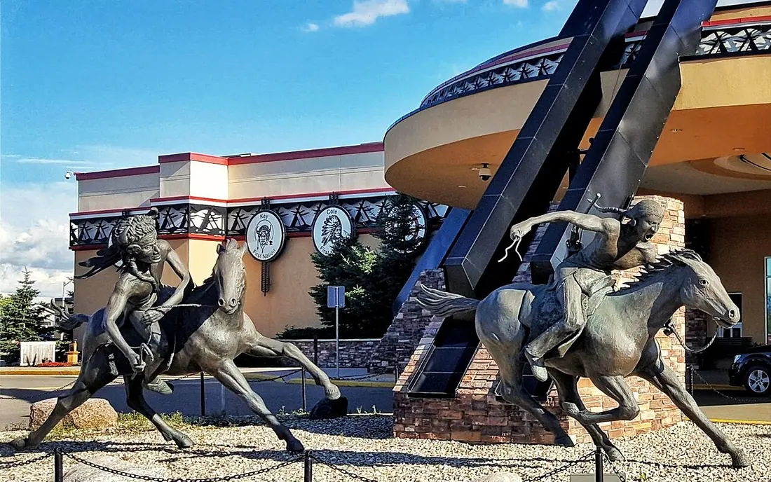 Bronze sculpture of riders on horseback in front of the curved entrance of Painted Hand Casino in Yorkton