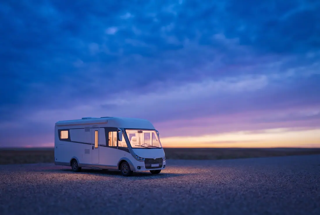 White motorhome parked alone on a gravel lot at dusk, its windows glowing warm