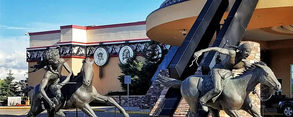 Bronze sculpture of riders on horseback in front of the curved entrance of Painted Hand Casino in Yorkton